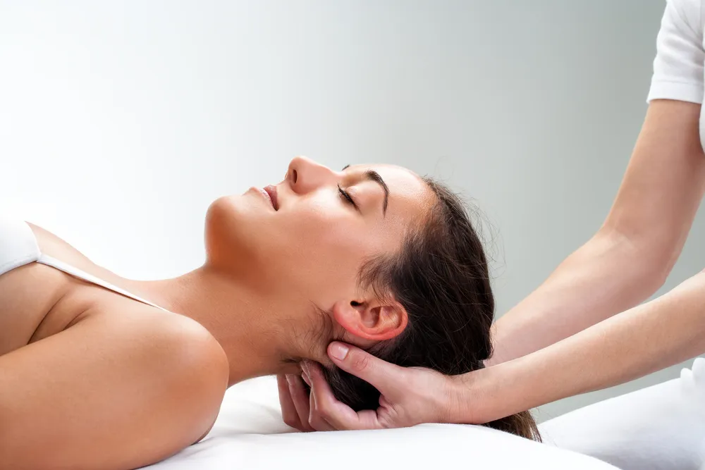 Close up of chiropractor pressing back of womans head. Therapist doing healing massage with fingers at back of neck.